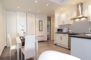 A modern kitchen with white cabinets, a microwave, and a dining area with white chairs and a table.