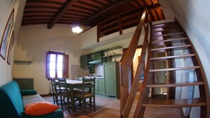 A cozy living room with a green sofa, a wooden staircase, and a kitchen area with green cabinets. - Residence Il Palazzo_Casa Arezzo (Pergine V.no, AR)
