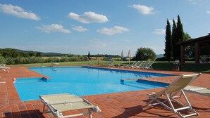 A rectangular swimming pool with clear blue water, surrounded by a brick patio. There are several lounge chairs and umbrellas around the pool area. - Residence Il Palazzo_Casa Arezzo (Pergine V.no, AR)