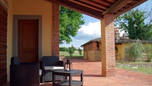 A covered patio with wicker furniture and a lantern, brick walls, and a view of the surrounding landscape. - Residence Il Palazzo_Casa Arezzo (Pergine V.no, AR)