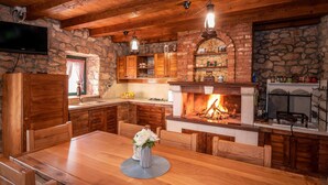 Eine rustikale Küche mit Steinwand, Holzschränken, Kamin und Essbereich mit Tisch und Stühlen.