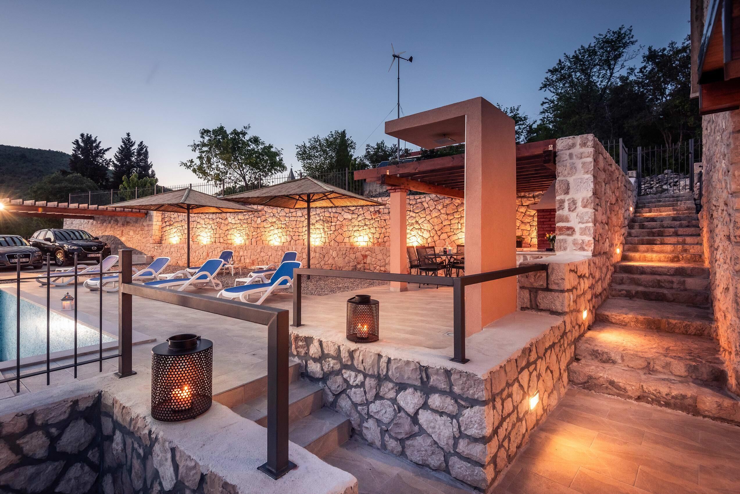 A poolside area with lounge chairs, a stone wall, and a staircase leading to an upper level.