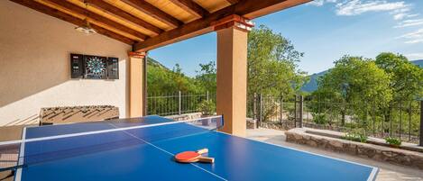 A ping pong table with two paddles and a net, under a wooden ceiling with a dartboard on the wall.
