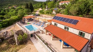 Eine Villa mit Swimmingpool, überdachter Sitzgelegenheit und Solaranlage.