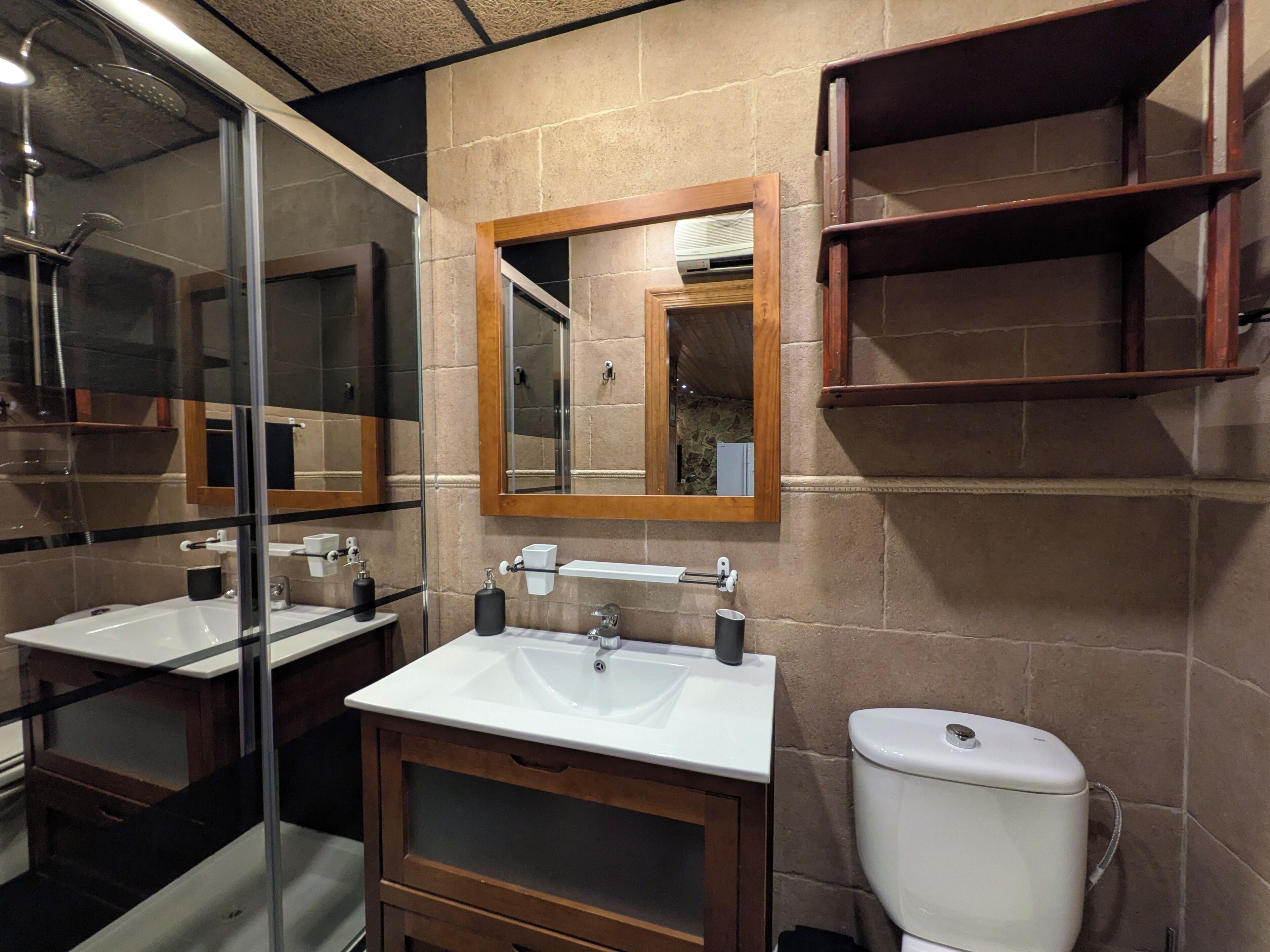 A bathroom with a glass shower enclosure, a white sink with a wooden vanity, a mirror, and a toilet.
