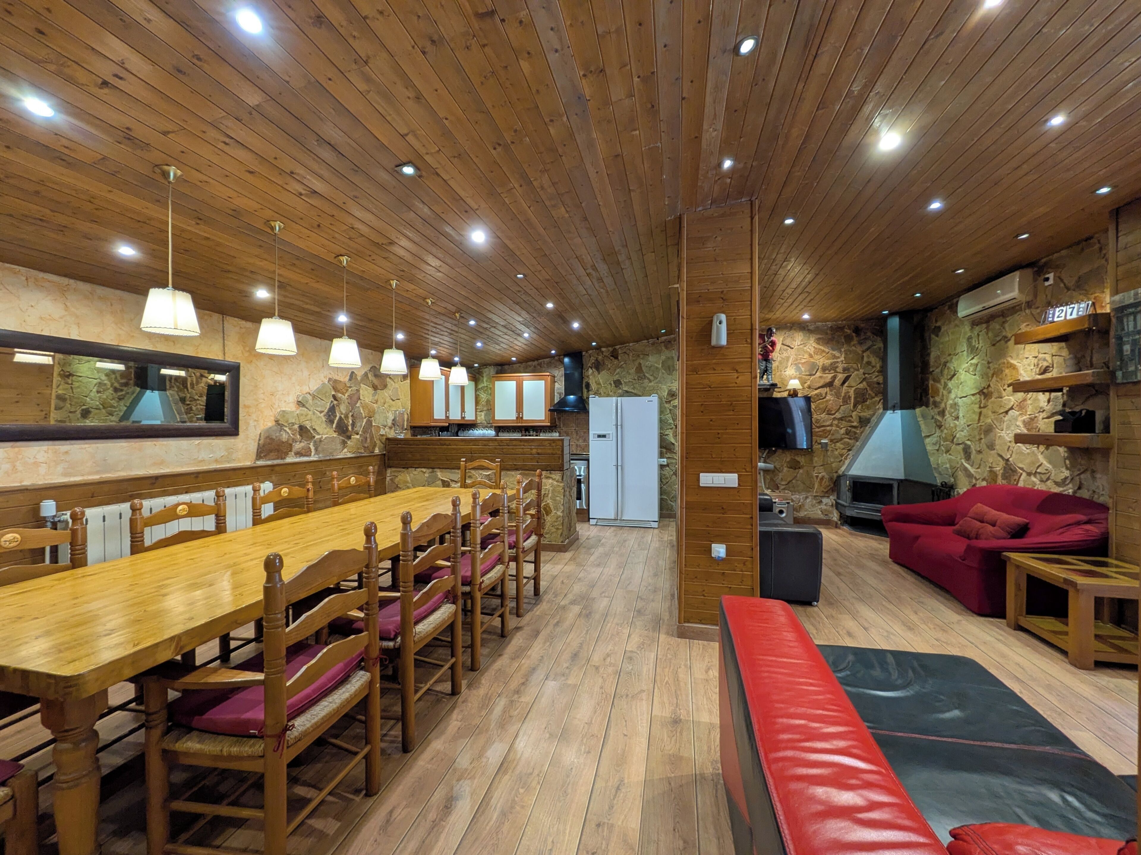 Una habitación con paneles de madera, una larga mesa de comedor, sillas, un sofá rojo y una pared de piedra.