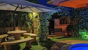 Ein Patio mit einer runden Tischgruppe, einer Bank und einem großen Sonnenschirm, der Schatten spendet.