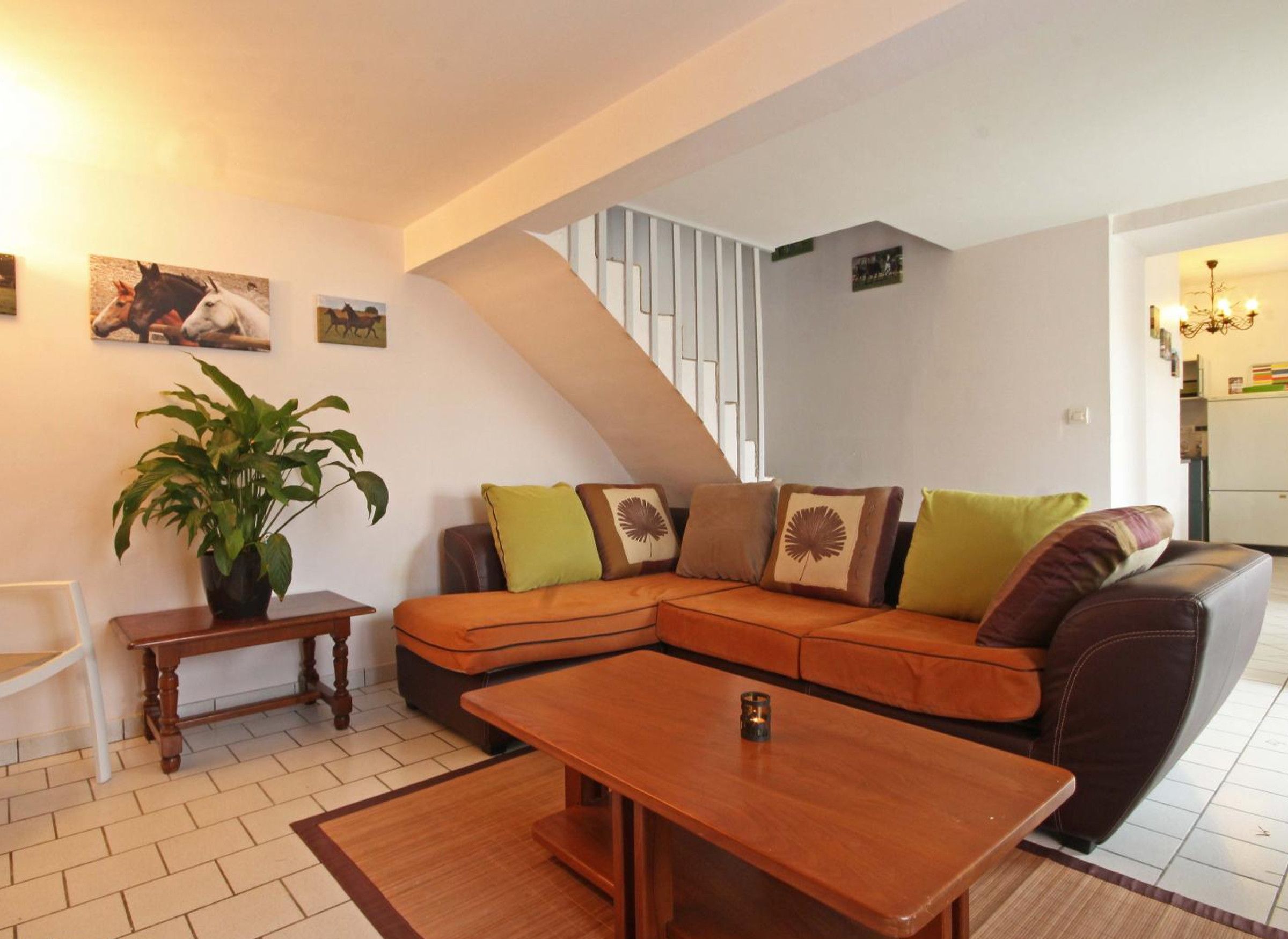 A cozy living room with a sectional sofa, a wooden coffee table, a potted plant, and a staircase leading to another level.