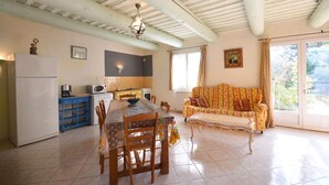 Una cocina con una mesa de comedor, sillas y un sofá. Incluye un refrigerador, microondas y una ventana con cortinas.