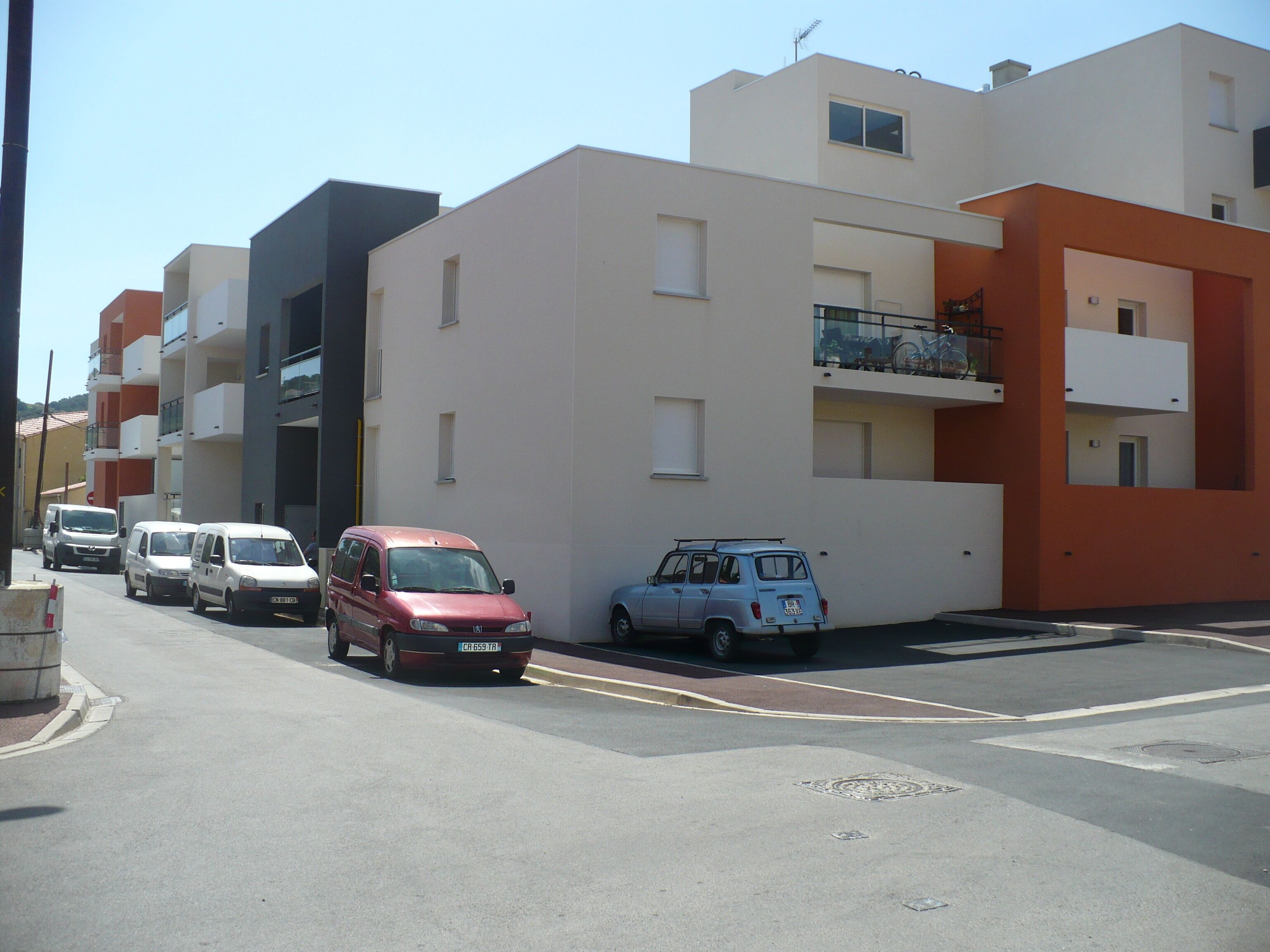 A street with modern buildings, parked cars, and a clear sky.