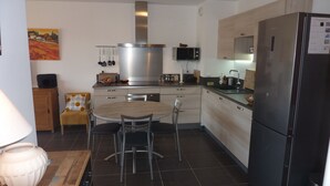 A modern kitchen with a large stove, microwave, and refrigerator. There is a dining table with chairs and a wooden cabinet.