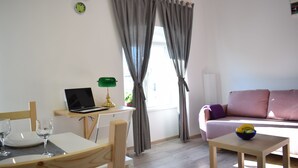 En moderne stue med en bærbar computer på et skrivebord, en sofa, et lille bord med en skål og et vindue med gardiner.
