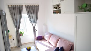 En stue med en lyserød sofa, et lille bord med en skål frugt og et vindue med gardiner.