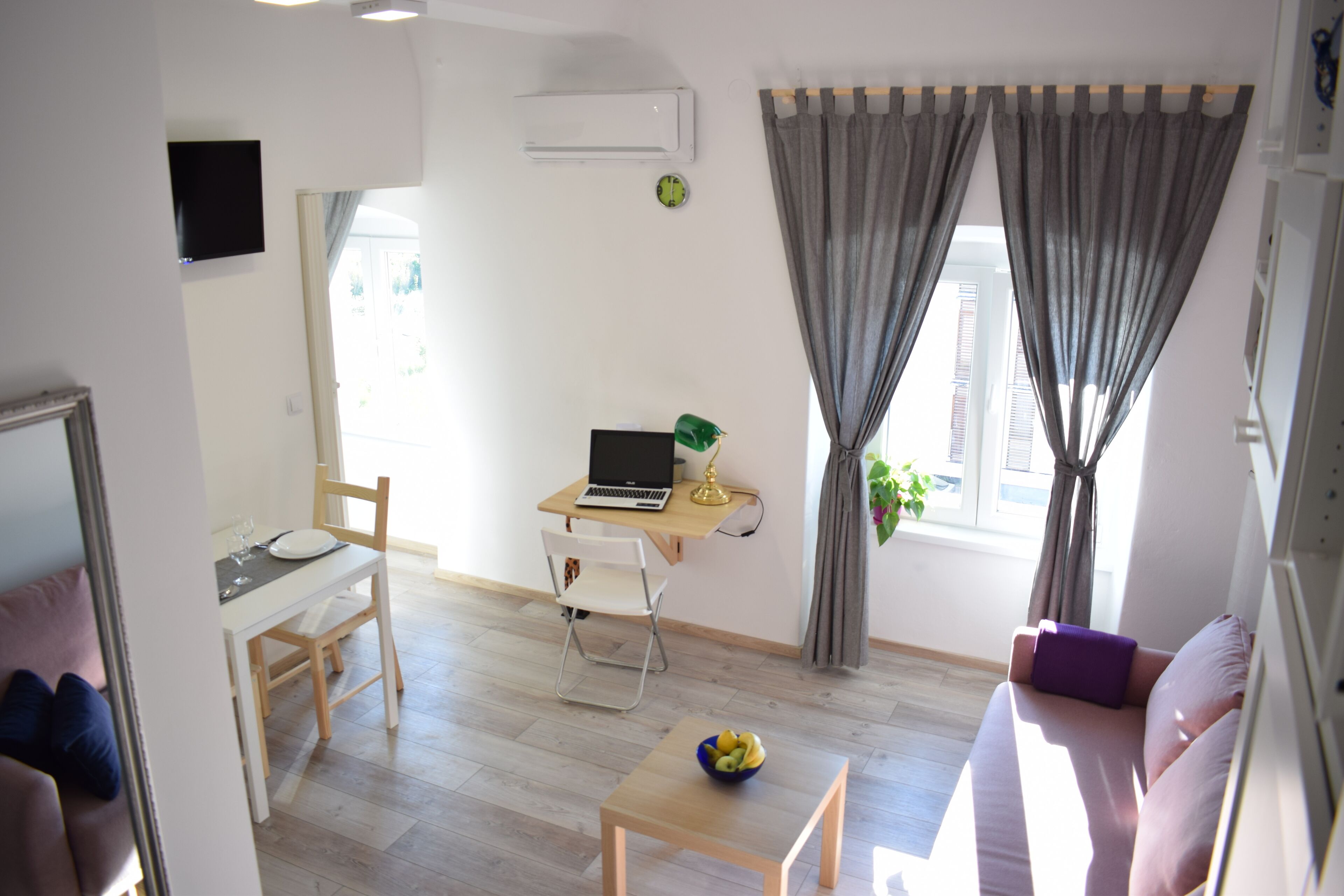 Un salon moderne avec un canapé, une table à manger, un ordinateur portable posé sur un bureau et une fenêtre avec des rideaux.