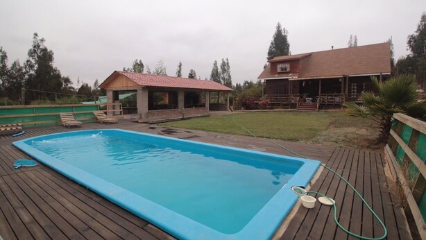 Una piscina con cubierta de madera, un porche techado y un jardín con césped.