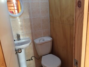 A small bathroom with a white sink, toilet, and wooden wall paneling. - Casa en Parcela (Zapallar)