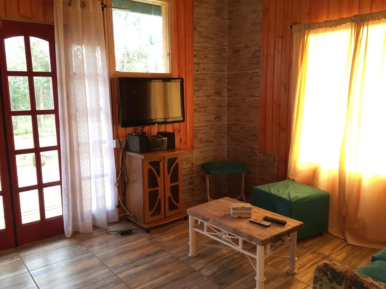 A cozy room with a wooden floor, a television on a cabinet, a small table, and a green sofa.