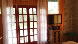 Una habitación con paredes de madera, un ventanal con cortinas, un televisor sobre un mueble y un banco de madera.