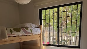 Une chambre de dortoir avec deux lits superposés, un petit bureau blanc avec une lampe et une fenêtre avec des barreaux en métal.