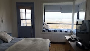 Une chambre à coucher avec un lit, un coin fenêtre donnant sur un beau paysage, une télévision et une porte.