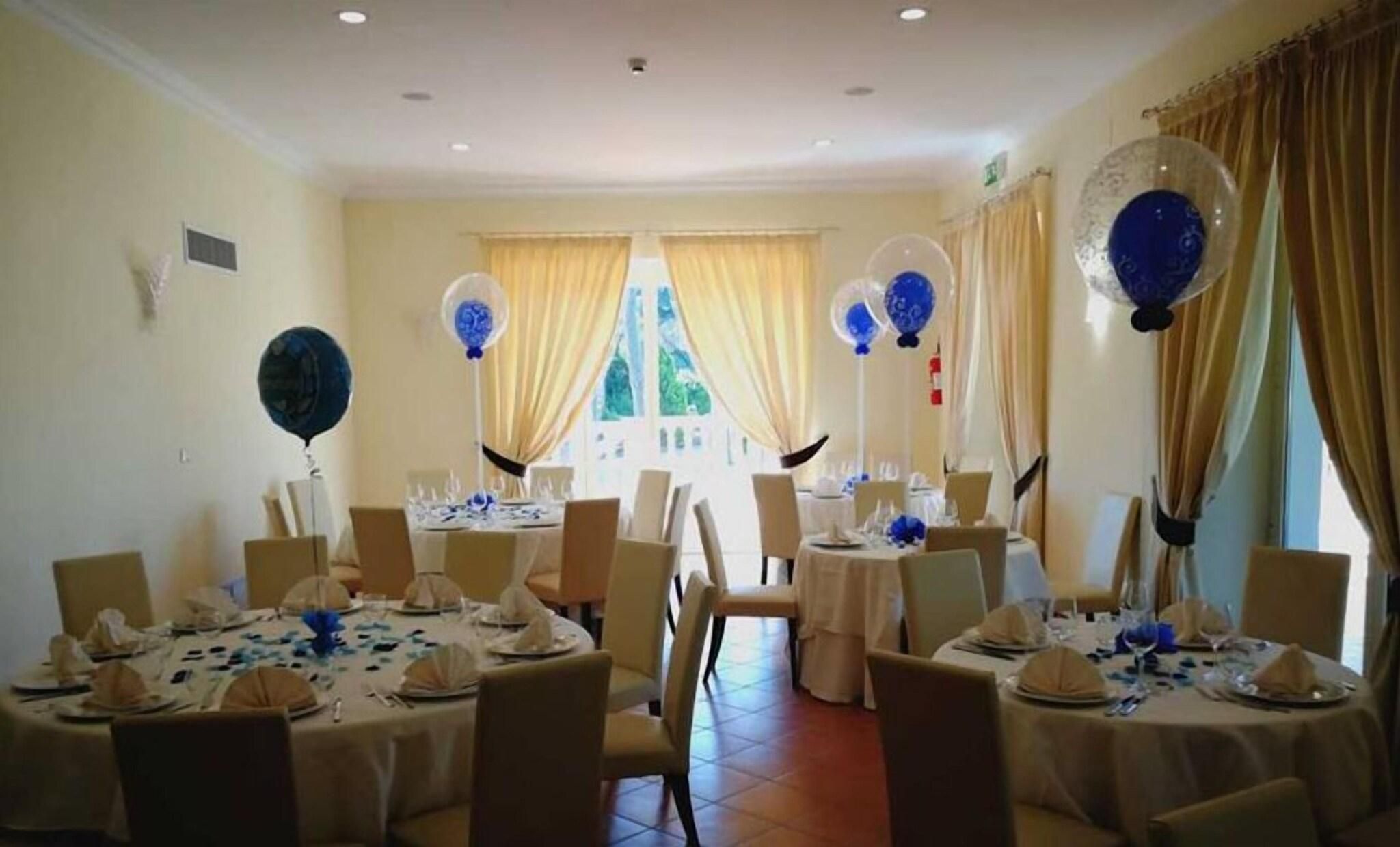 A banquet hall with round tables set for dining, featuring blue and white tablecloths and balloons.