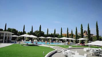 Area piscina con ombrelloni bianchi, lettini e prato.