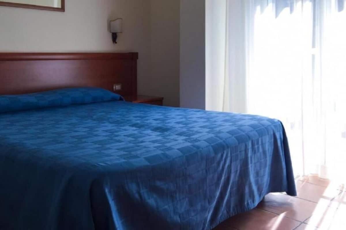 A single bed with a wooden headboard, a nightstand, and a wall-mounted lamp.
