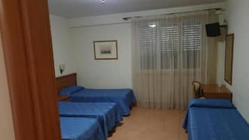 A room with three single beds, a wooden desk, a chair, a television, and a window with curtains.