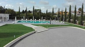 A swimming pool with lounge chairs, a grassy area, and a curved pathway. - Villamaria Park Hotel (Albano Laziale)
