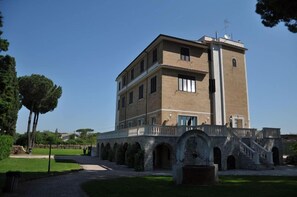 Un edificio de varios pisos con una torre central, rodeado por un patio con arcos y un sendero.