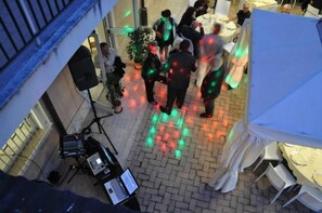 An outdoor event area with a DJ setup, tables, and chairs, surrounded by a brick wall and a glass door. - Villamaria Park Hotel (Albano Laziale)