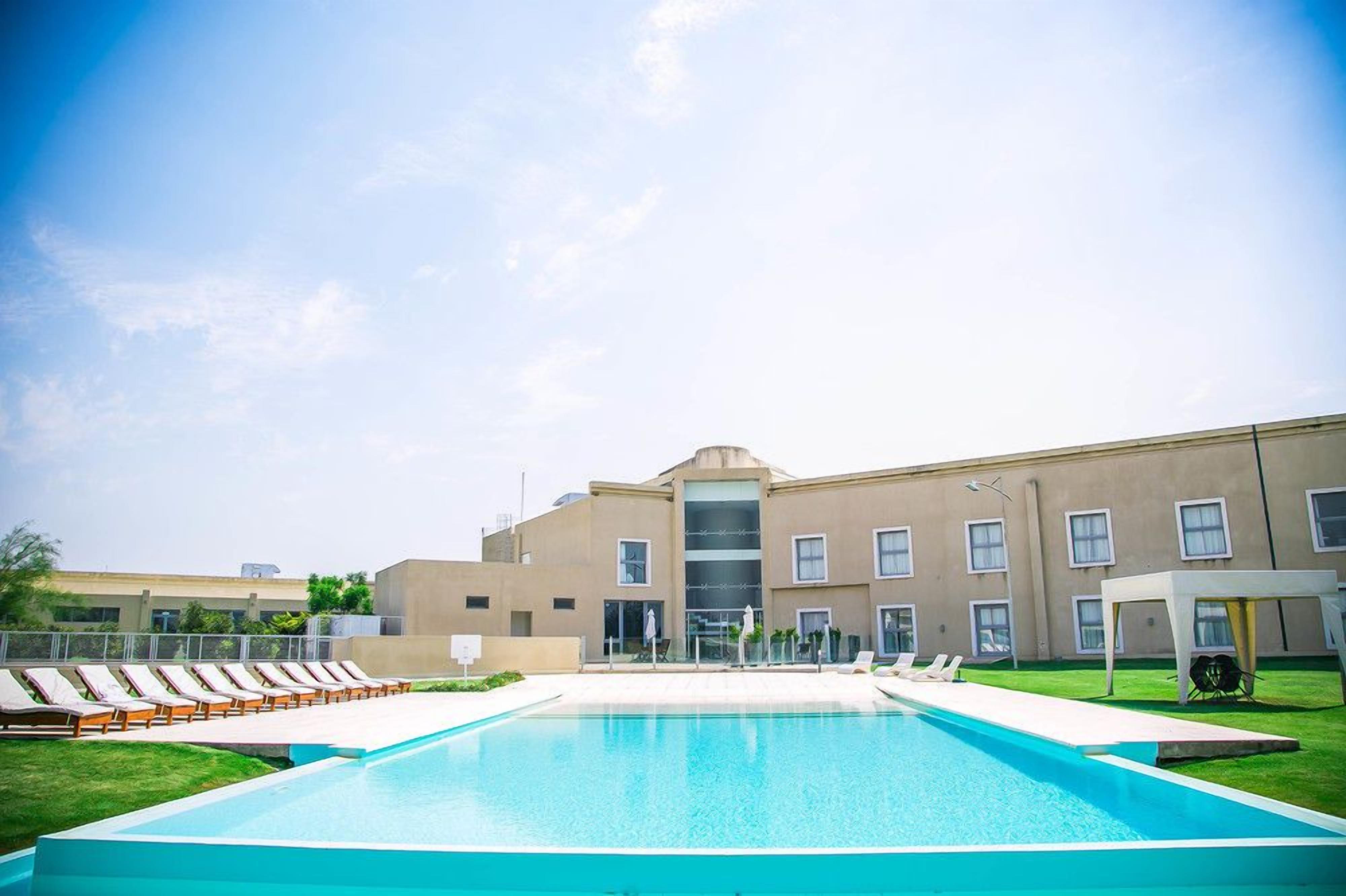 Ein Schwimmbecken mit Liegestühlen und ein Gebäude mit mehreren Fenstern und einem zentralen Eingang.