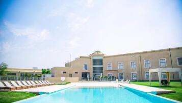 Ein Schwimmbecken mit Liegestühlen und ein Gebäude mit mehreren Fenstern und einem zentralen Eingang.