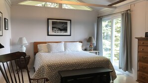 A bedroom with a bed, a nightstand, a lamp, a wooden dresser, a bench, and a framed picture on the wall. - Relaxing ocean front property with picturesque harbor views (Addison)