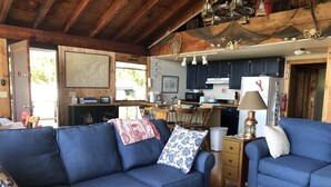 A cozy living room with blue sofas, a wooden coffee table, and a kitchen area with dark cabinets and a microwave. - Relaxing ocean front property with picturesque harbor views (Addison)