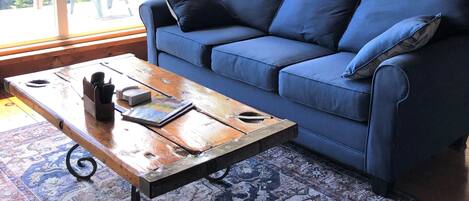 Ein gemütliches Wohnzimmer mit einem blauen Sofa, einem Holztisch und einem gemusterten Teppich.