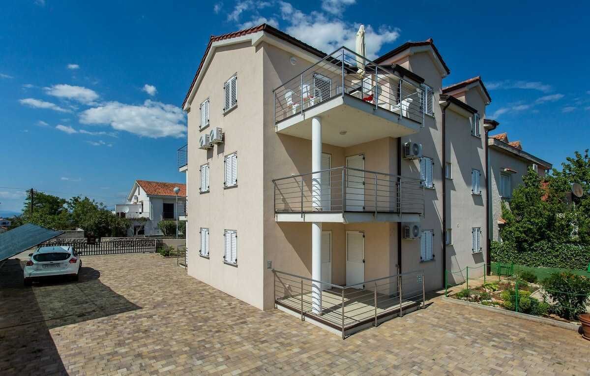 Un immeuble résidentiel à plusieurs étages, doté de balcons, d’une allée pavée et d’une voiture garée devant.