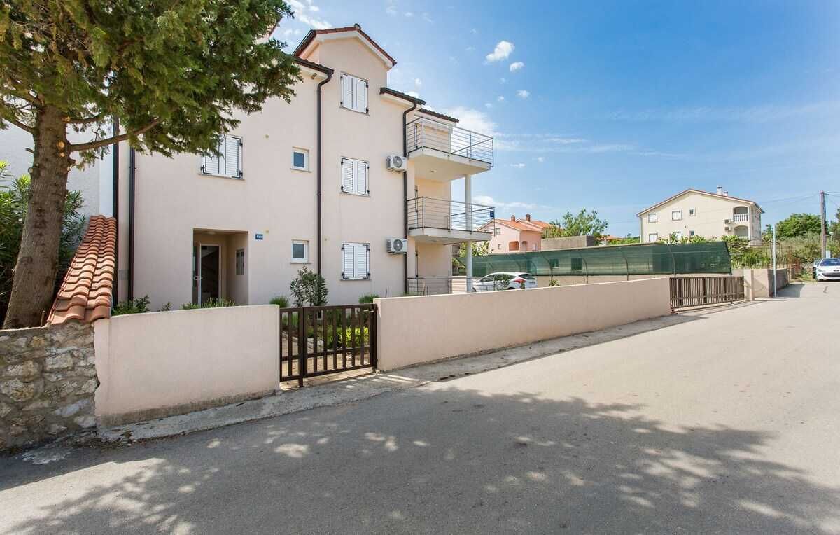 Un edificio residencial de varios pisos con un balcón, una entrada protegida por un portón y un cielo despejado.
