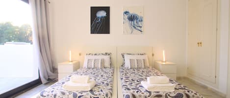 Un lit double avec une couvre-lit à motifs, deux lampes de chevet et deux œuvres d’art murales représentant des méduses.