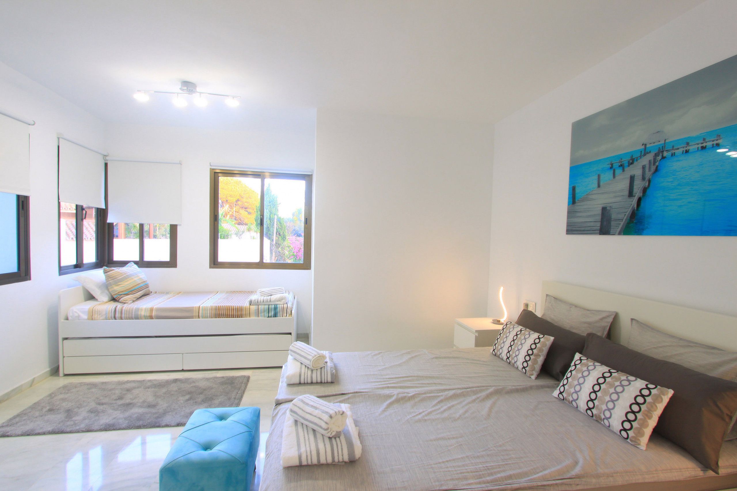 Een moderne slaapkamer met een groot bed, een slaapbank, een klein tafeltje en een schilderij aan de muur.