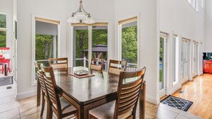 Een ruime eethoek met een grote houten tafel en stoelen, grote ramen en uitzicht op het landschap.