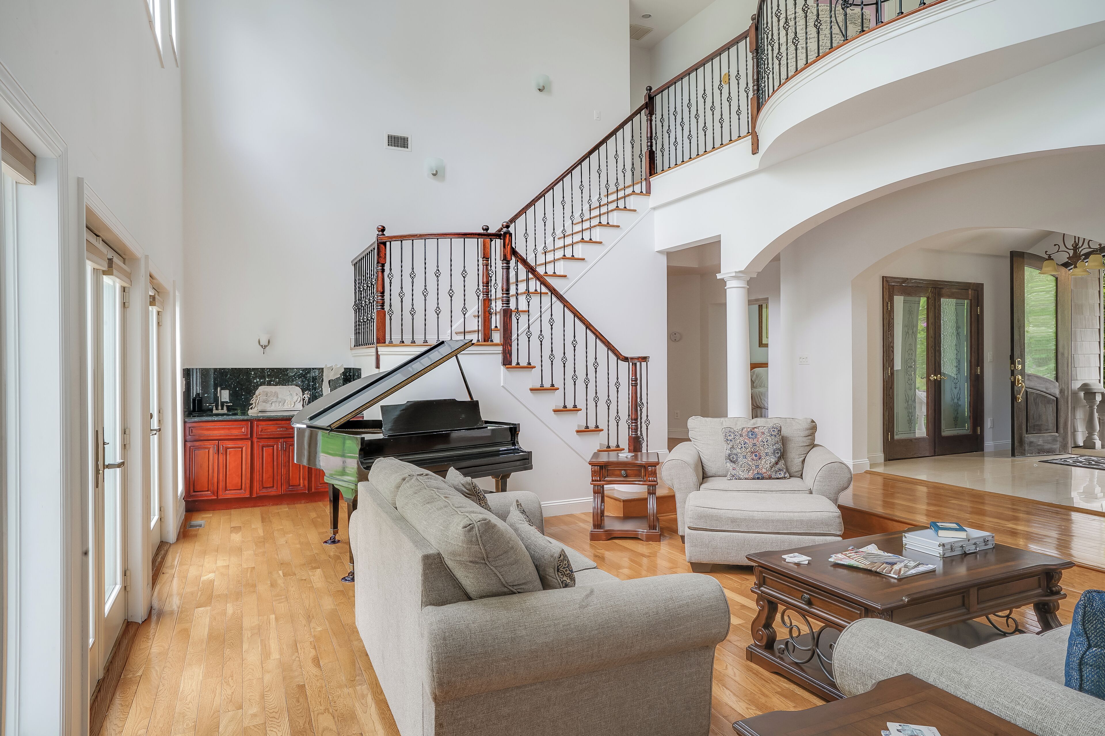A spacious living room with a grand piano, a staircase, and a cozy seating area.