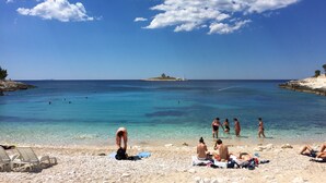 A beach with clear turquoise water, people sunbathing and swimming, and a distant island. - Outdoor oasis -apartment, close to center of Hvar (Hvar)