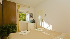 A bedroom with a bed, a nightstand, a potted plant, a window with curtains, and a door. - Outdoor oasis -apartment, close to center of Hvar (Hvar)