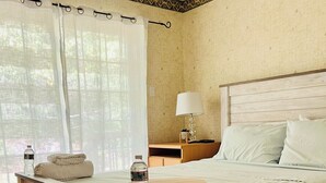 A wooden bed with a beige mattress, a bedside table with a lamp, and a window with sheer curtains. - Lake House Private Waterfront - Lake & Beach life in Winnipesaukee (Laconia)