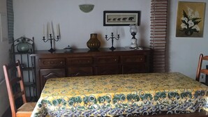 Une table à manger en bois, recouverte d’une nappe à motifs, agrémentée d’un chandelier et ornée d’un tableau encadré au mur.