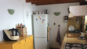 Une cuisine de taille réduite, avec un réfrigérateur blanc, des meubles de rangement jaunes, une cuisinière à gaz et un petit évier.