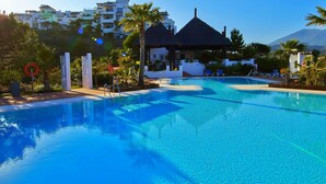 Ein klares, blaues Schwimmbecken mit einem strohgedeckten Pavillon, Liegestühlen und Palmen.