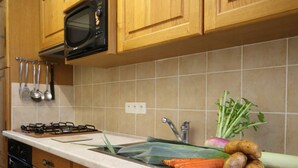 Una cocina con armarios de madera, microondas, estufa a gas y un fregadero. Hay verduras como zanahorias y patatas en la encimera.