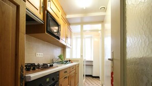 Una cocina compacta con armarios de madera, un microondas, una estufa y suelo de baldosas.